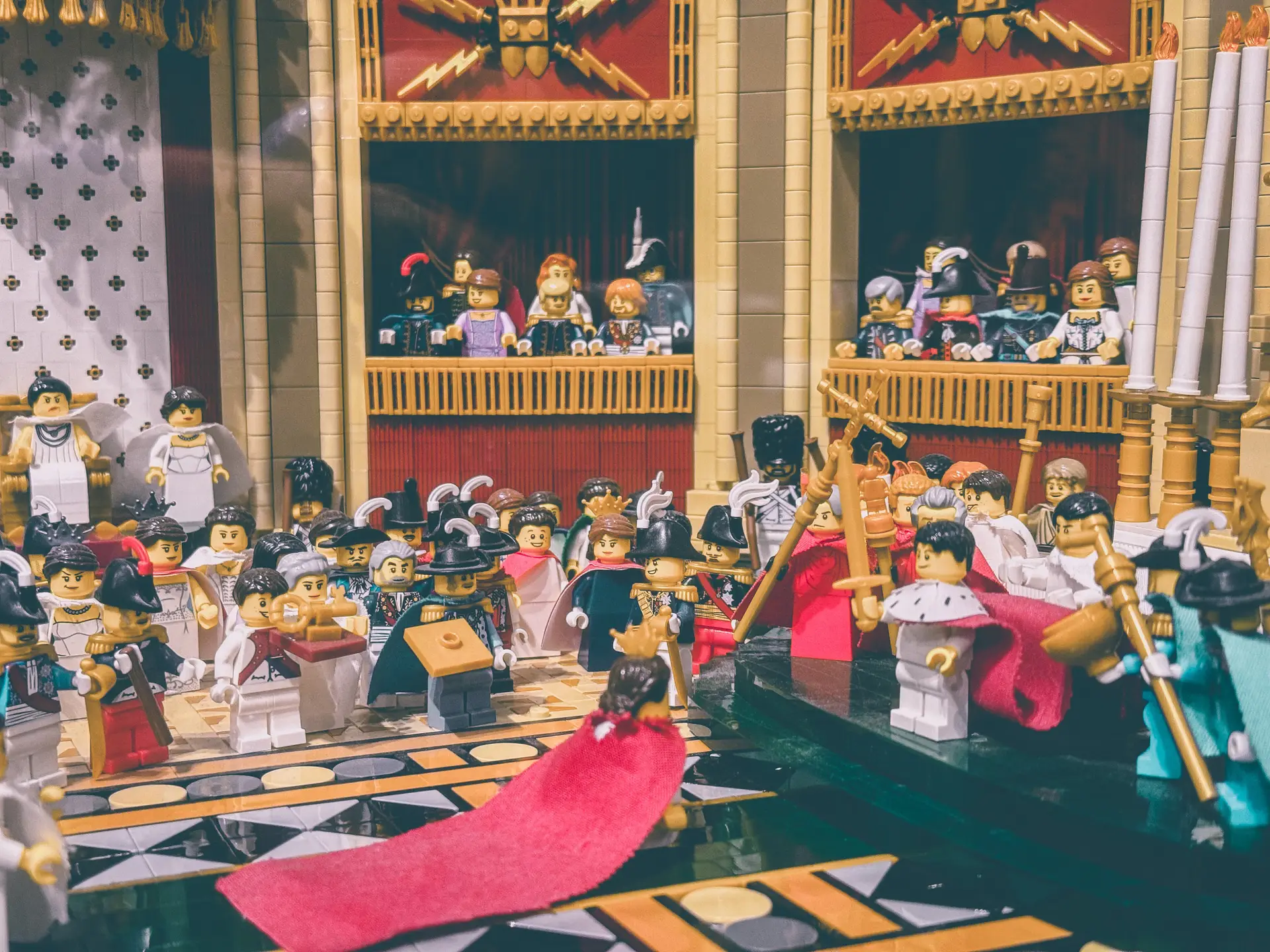 LEGO coronation diorama seen from the side, spectators packed into the tiered galleries above the ceremony.