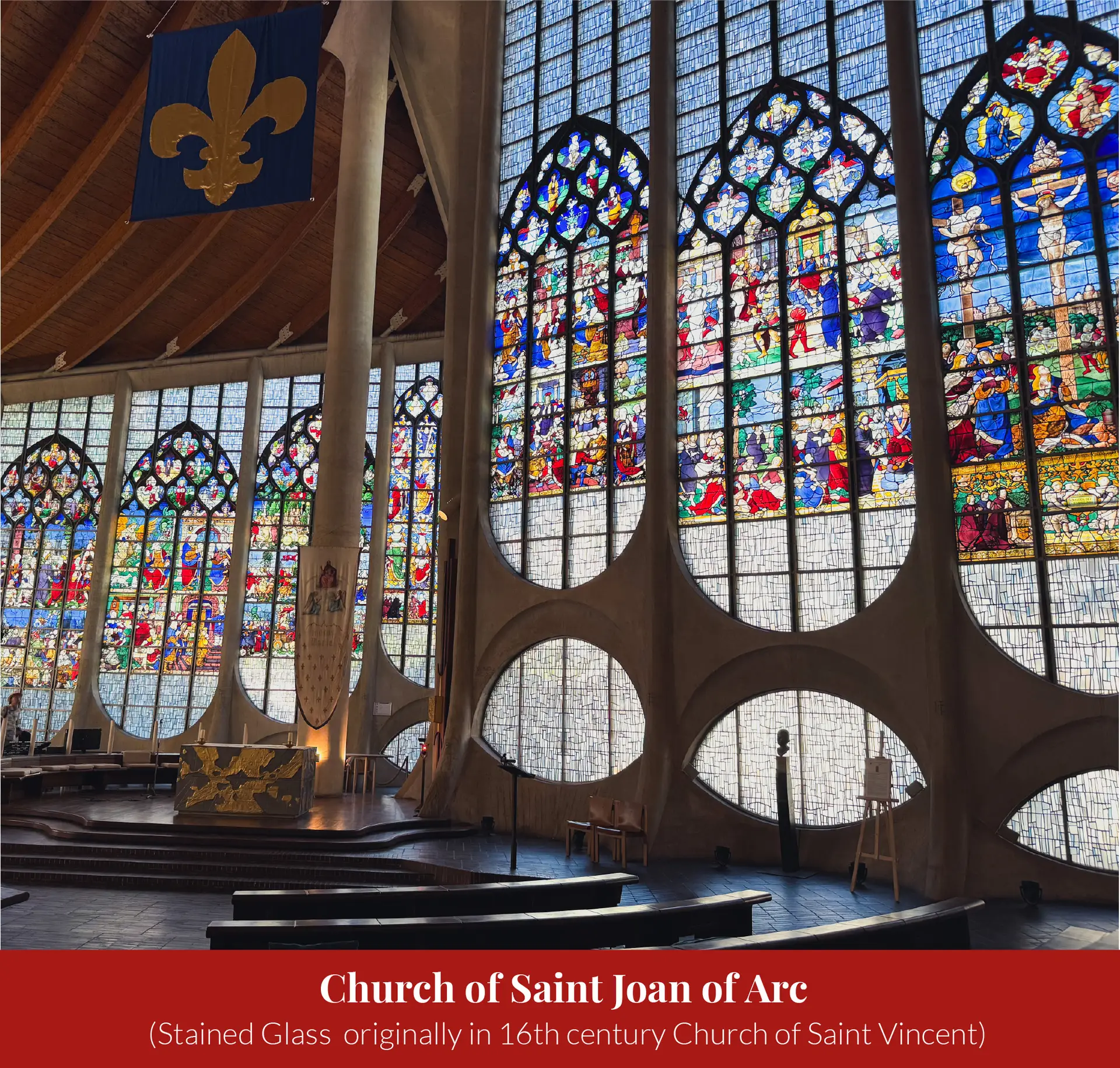 Interior of the Church of Saint Joan of Arc showing tall panels of colourful 16th-century stained glass salvaged from the destroyed Church of Saint Vincent, with wooden pews below.