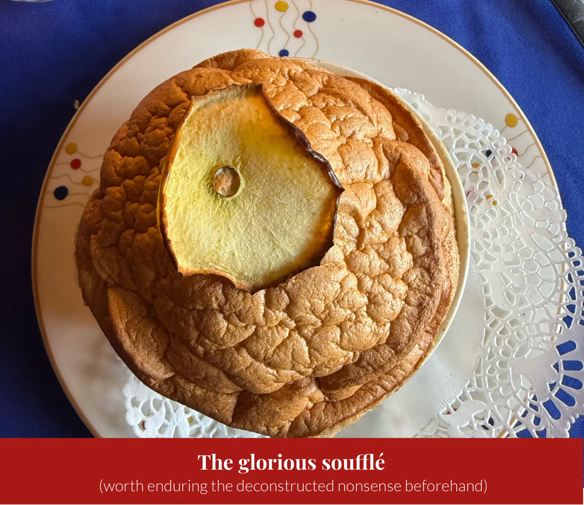 A puffed golden soufflxc3xa9 on a plate, split open to reveal a caramelised apple slice at its base.
