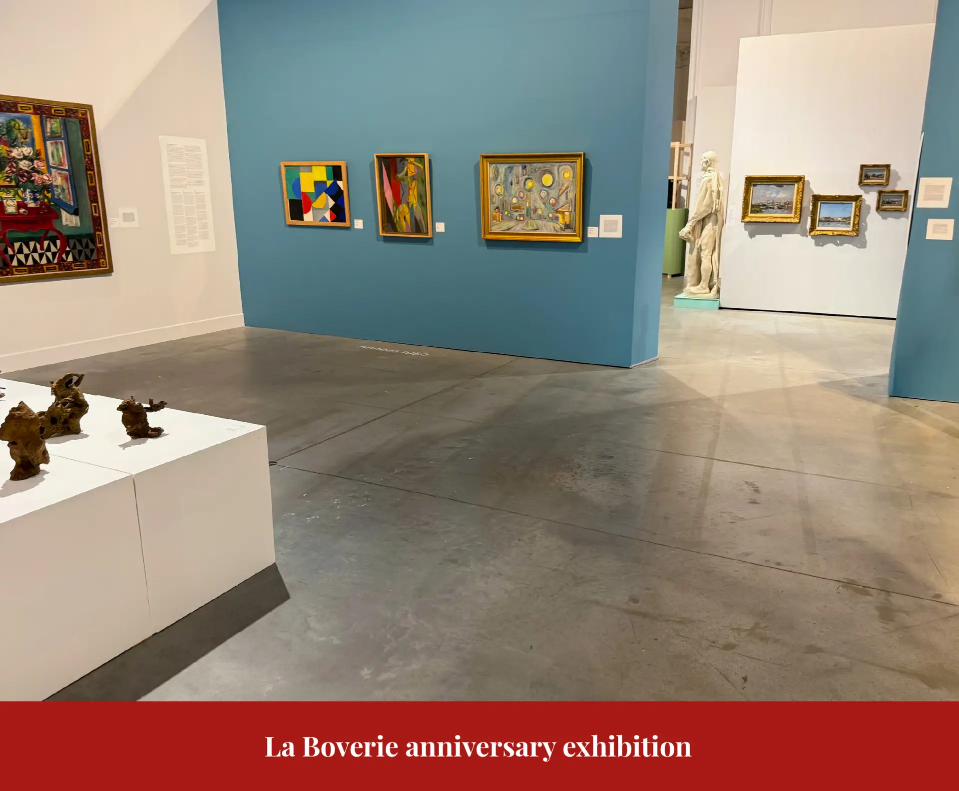 Gallery at La Boverie with modern paintings hung on a blue wall and small bronzes displayed on a plinth.