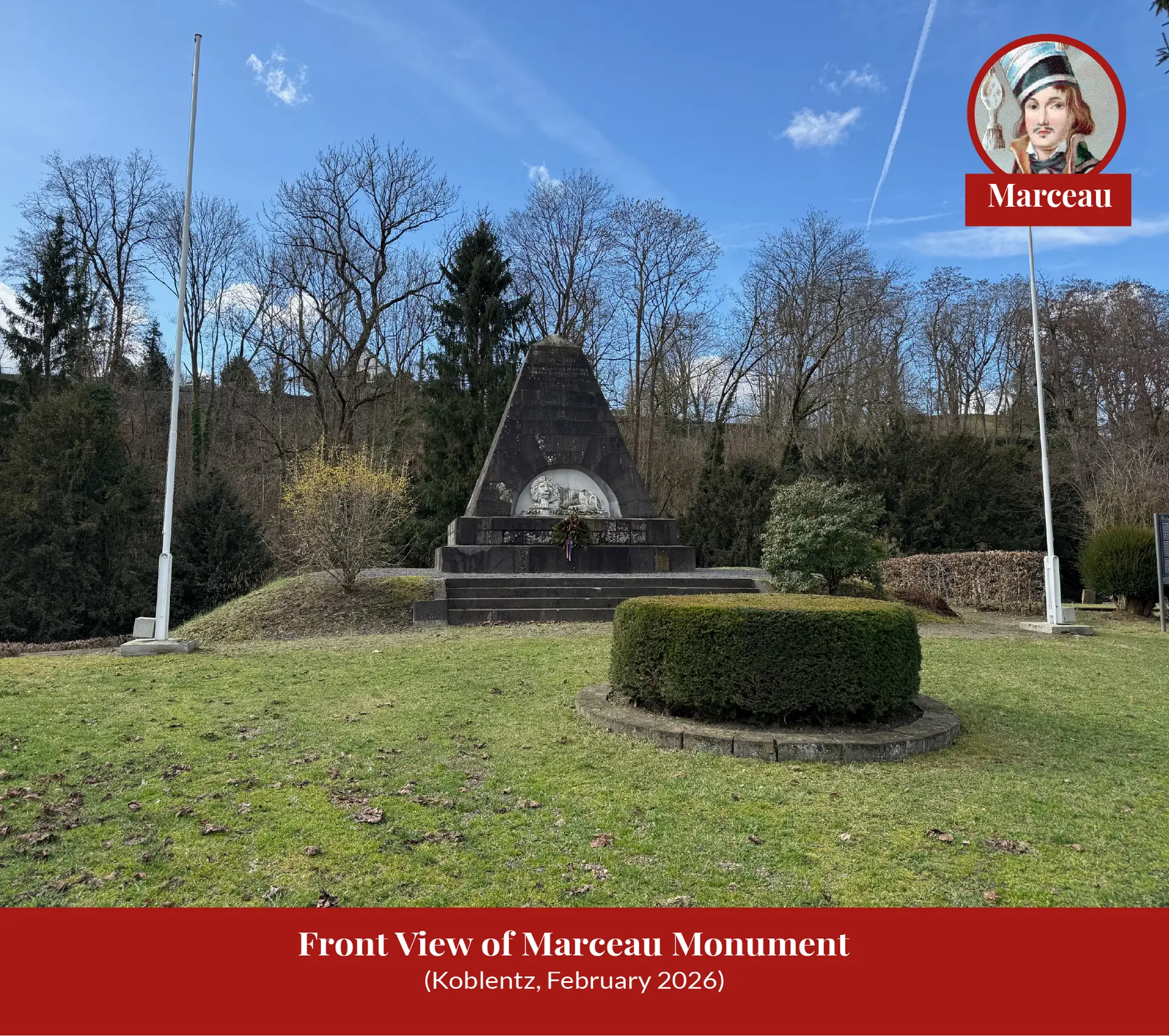 Wide view of the Marceau monument at Koblenz standing on a lawn between two flagpoles, with bare winter trees behind.